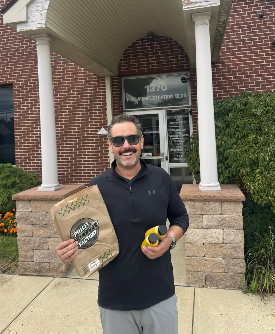 Eric, the owner of Titan East Roofing, smiling outside a fire department building with a bag of treats