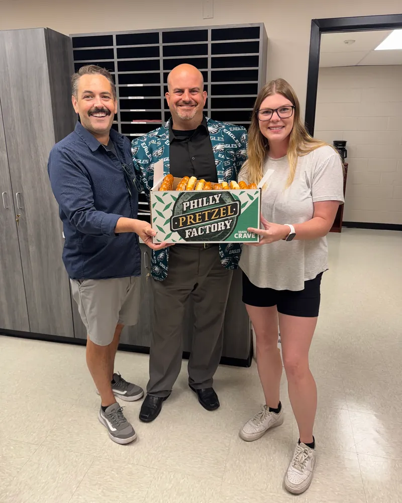 Eric, a teammate and a school staff member holding a box of soft pretzels
