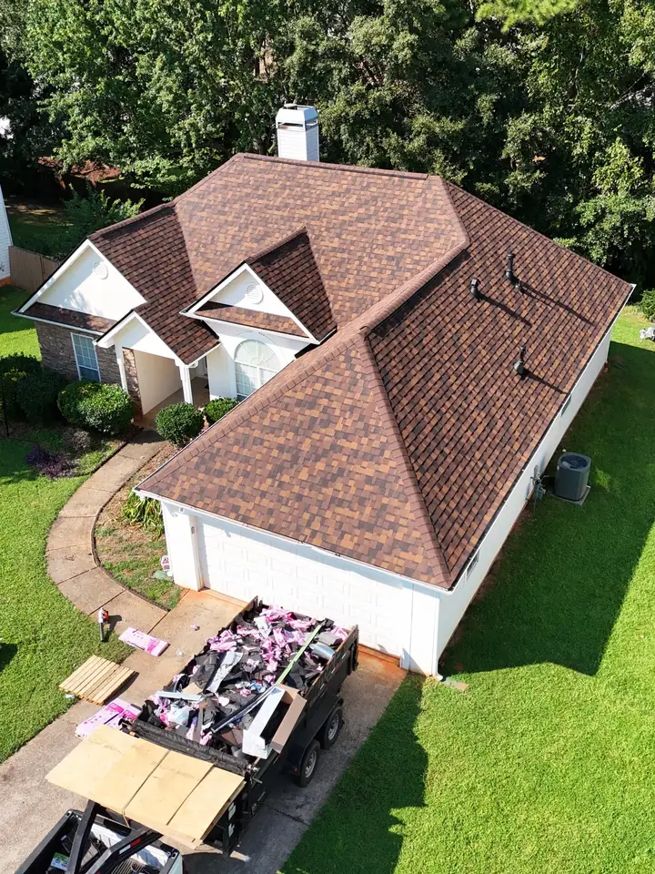 A new brown roof on a home, with a trailer of roofing materials in the driveway