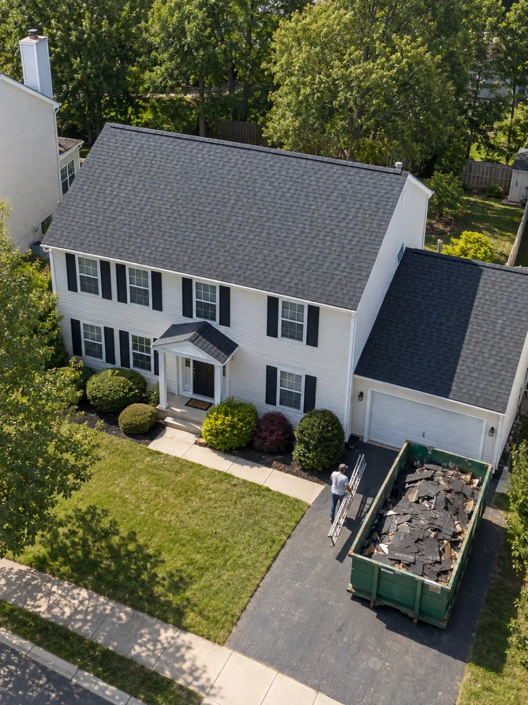 A new gray roof on a two-story home, with the old shingles in a dumpster in the driveway