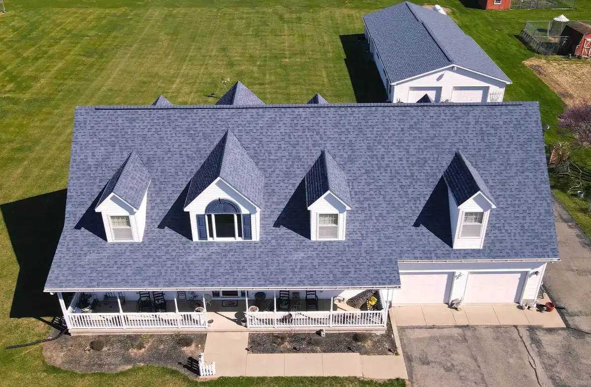 New blue-gray roof on a home with three dormers and a wraparound porch